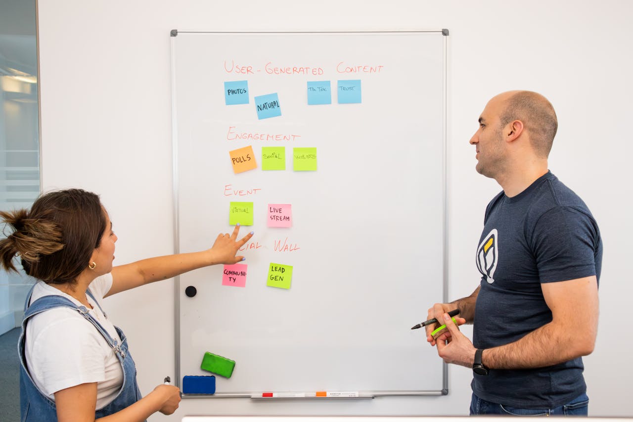 Two professionals brainstorming and planning projects on a whiteboard in a collaborative office setting.